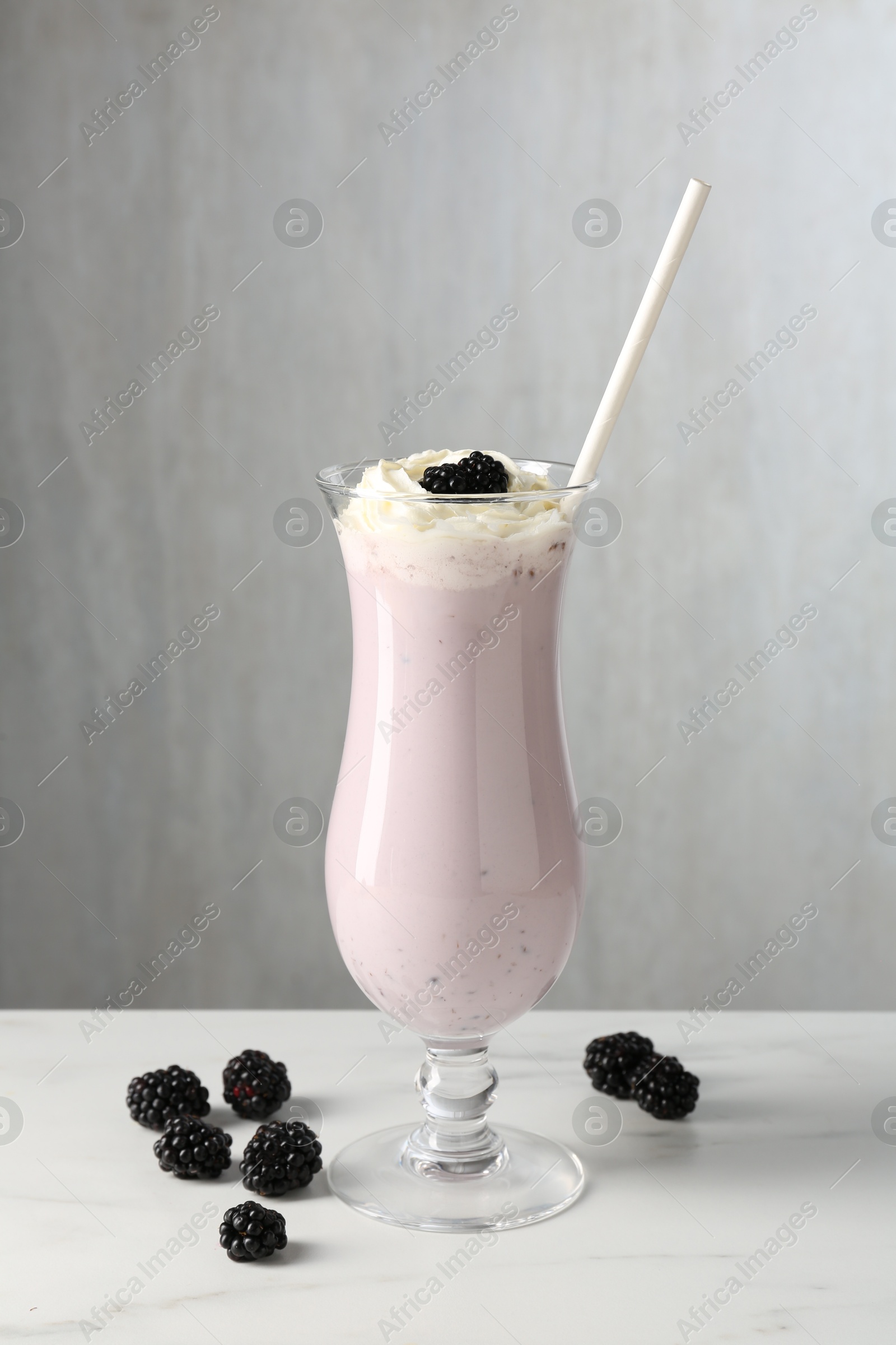 Photo of Tasty blackberry milkshake with whipped cream in glass and berries on white marble table