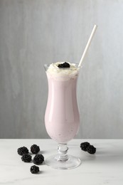 Photo of Tasty blackberry milkshake with whipped cream in glass and berries on white marble table