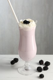 Photo of Tasty blackberry milkshake with whipped cream in glass and berries on white marble table