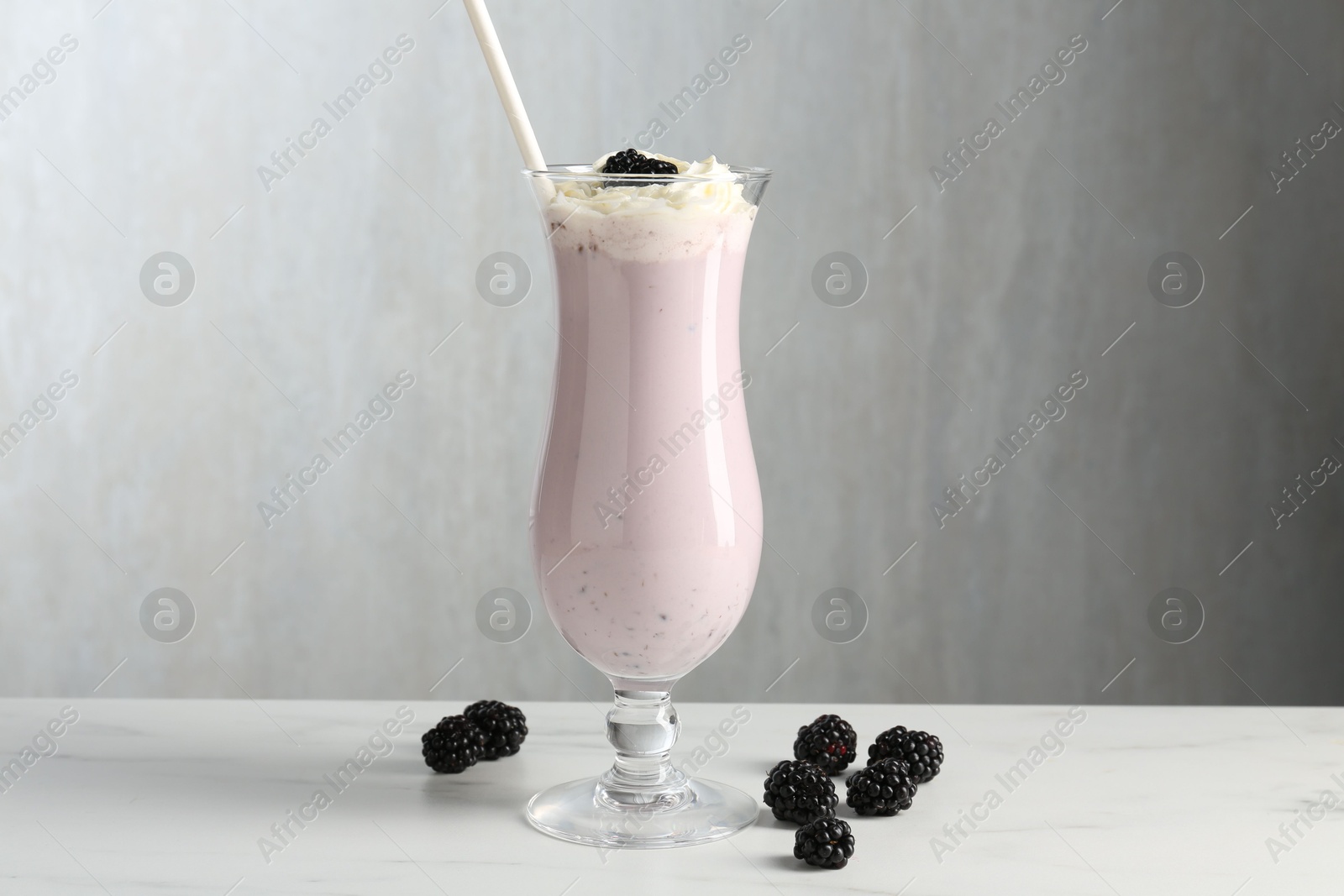 Photo of Tasty blackberry milkshake with whipped cream in glass and berries on white marble table