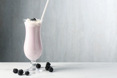 Photo of Tasty blackberry milkshake with whipped cream in glass and berries on white marble table, space for text
