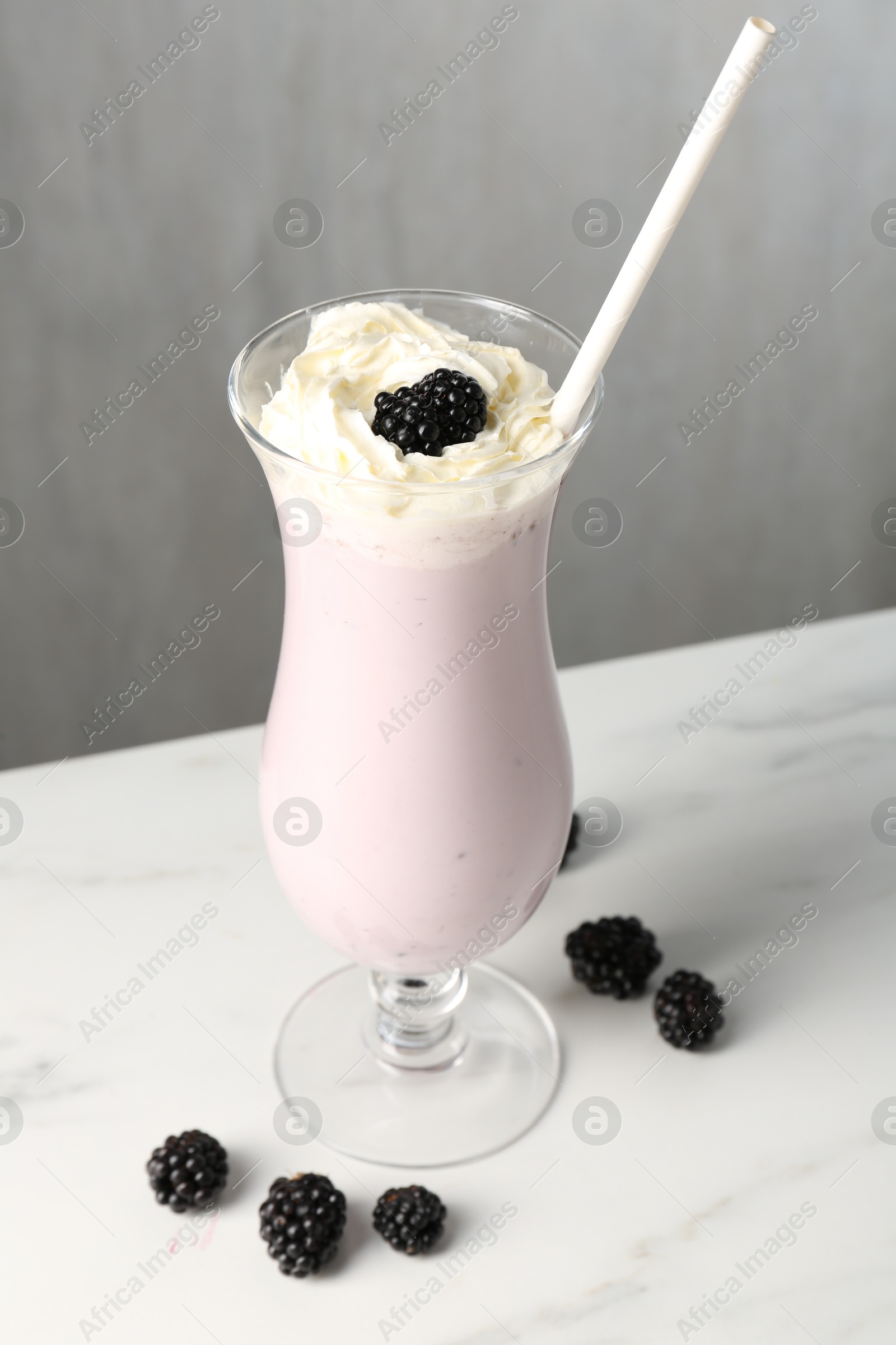 Photo of Tasty blackberry milkshake with whipped cream in glass and berries on white marble table