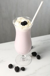 Photo of Tasty blackberry milkshake with whipped cream in glass and berries on white marble table