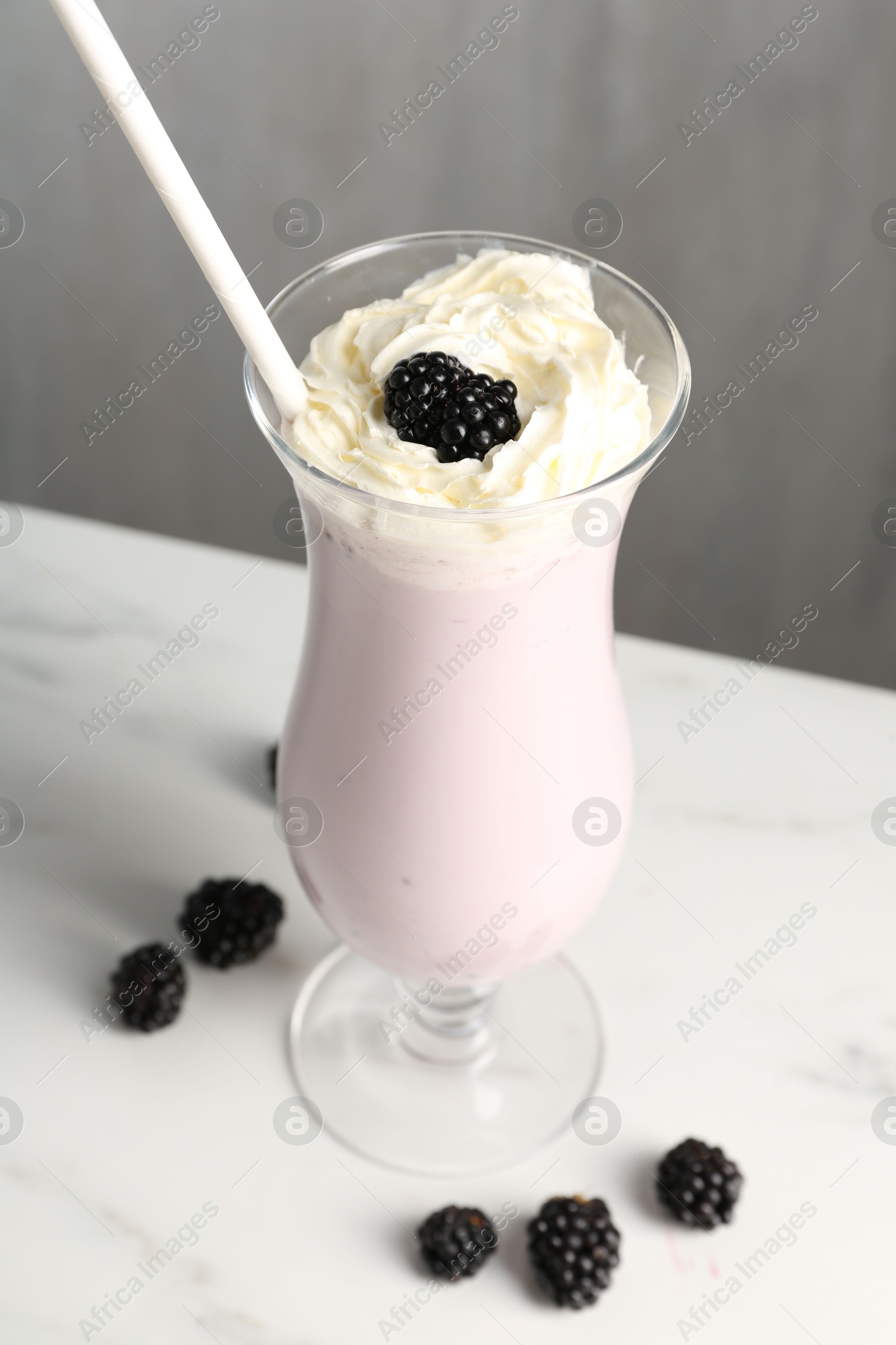 Photo of Tasty blackberry milkshake with whipped cream in glass and berries on white marble table, closeup