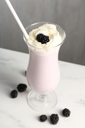 Photo of Tasty blackberry milkshake with whipped cream in glass and berries on white marble table, closeup