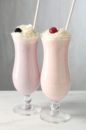 Photo of Different tasty milkshakes with whipped cream in glasses and berries on white marble table