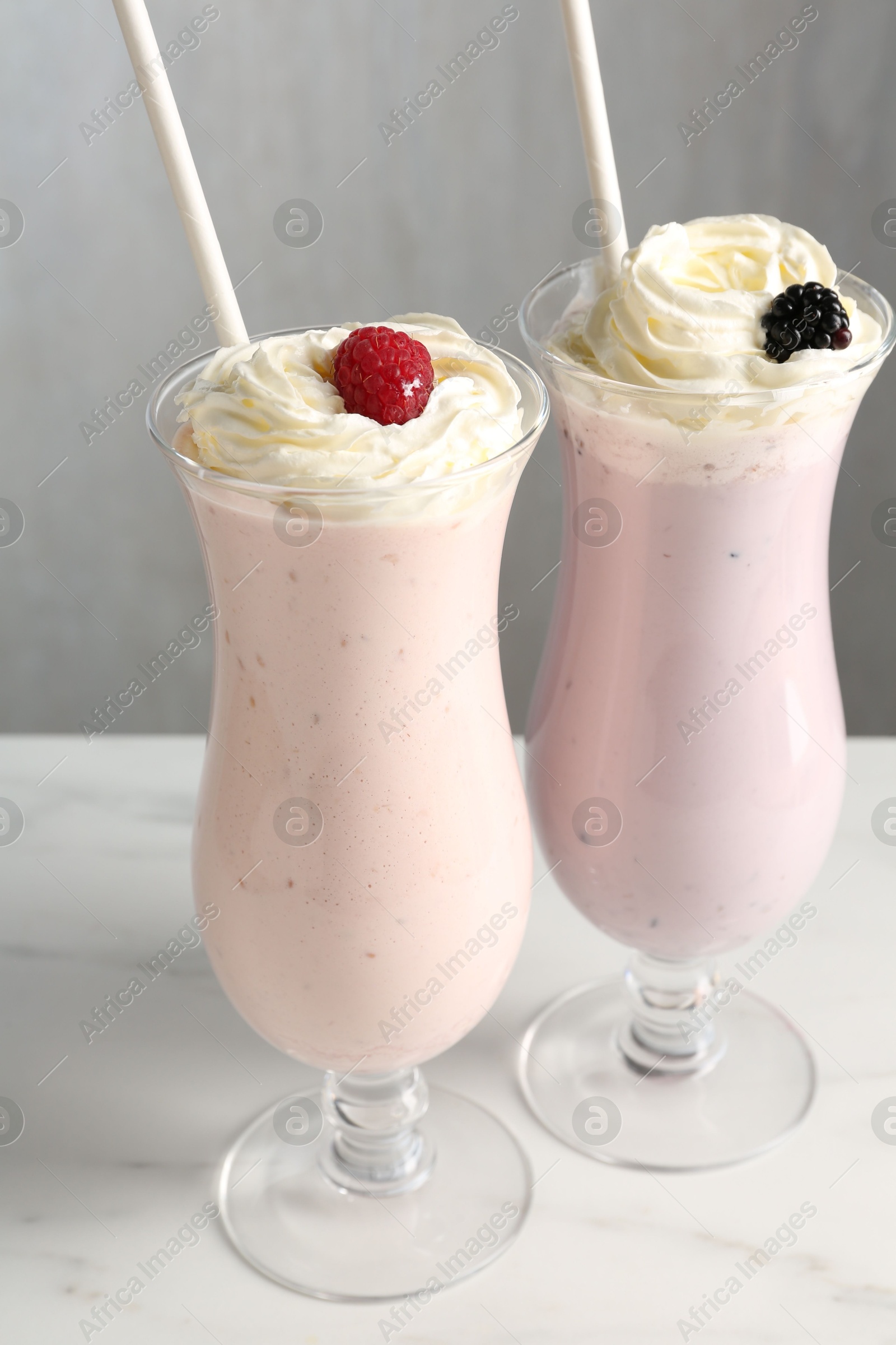 Photo of Different tasty milkshakes with whipped cream in glasses and berries on white marble table