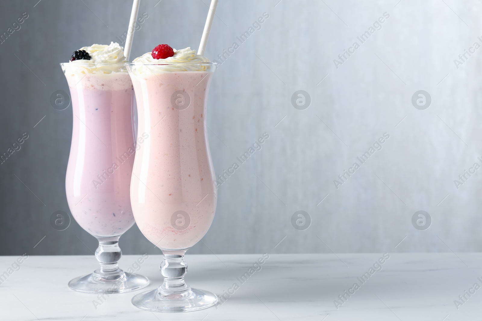 Photo of Different tasty milkshakes with whipped cream in glasses and berries on white marble table, space for text