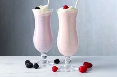 Photo of Different tasty milkshakes with whipped cream in glasses and berries on white marble table
