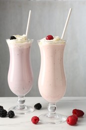 Photo of Different tasty milkshakes with whipped cream in glasses and berries on white marble table