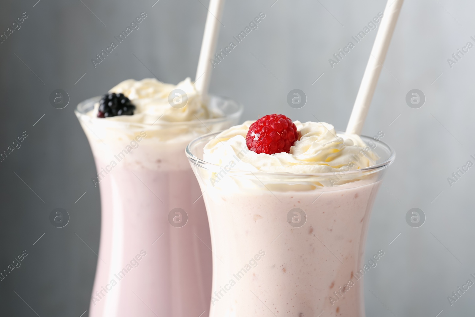 Photo of Different tasty milkshakes with whipped cream in glasses and berries on grey background, closeup