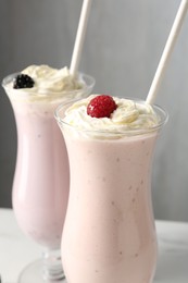 Photo of Different tasty milkshakes with whipped cream in glasses and berries on white table, closeup