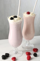 Photo of Different tasty milkshakes with whipped cream in glasses and berries on white marble table