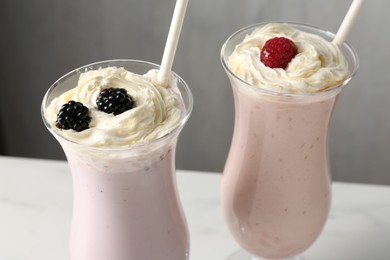 Photo of Different tasty milkshakes with whipped cream in glasses and berries on white table, closeup