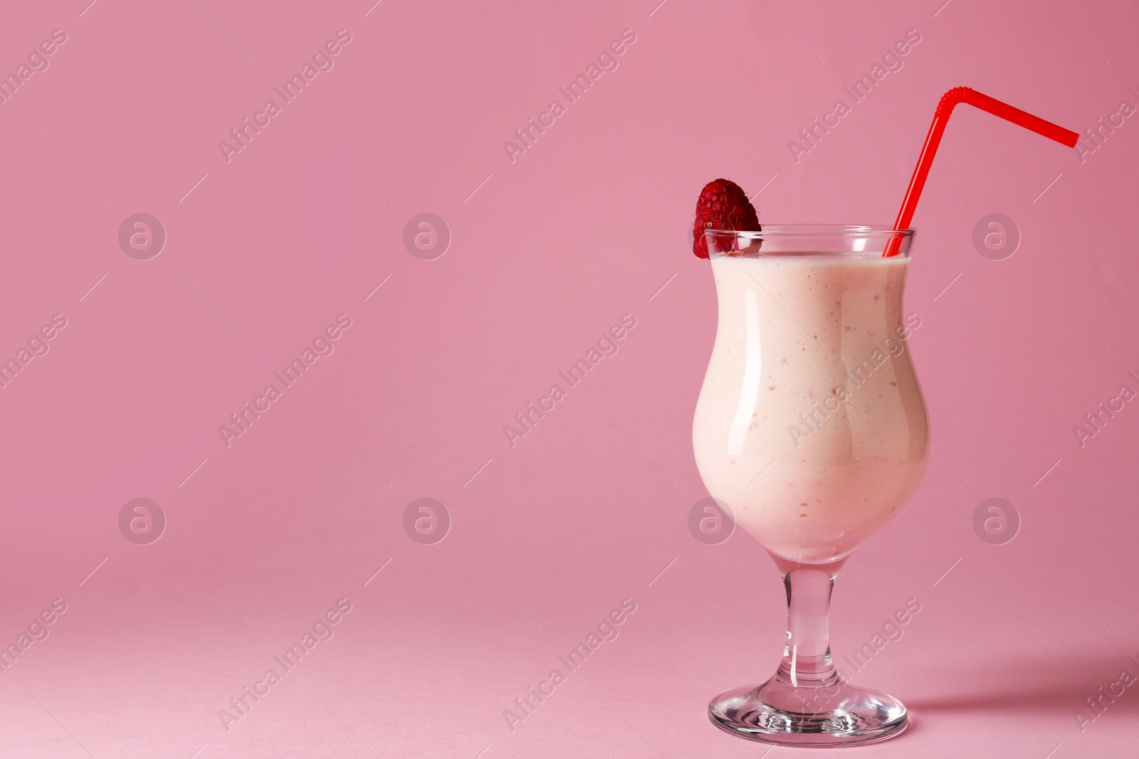 Photo of Tasty raspberry milkshake in glass on pink background, space for text