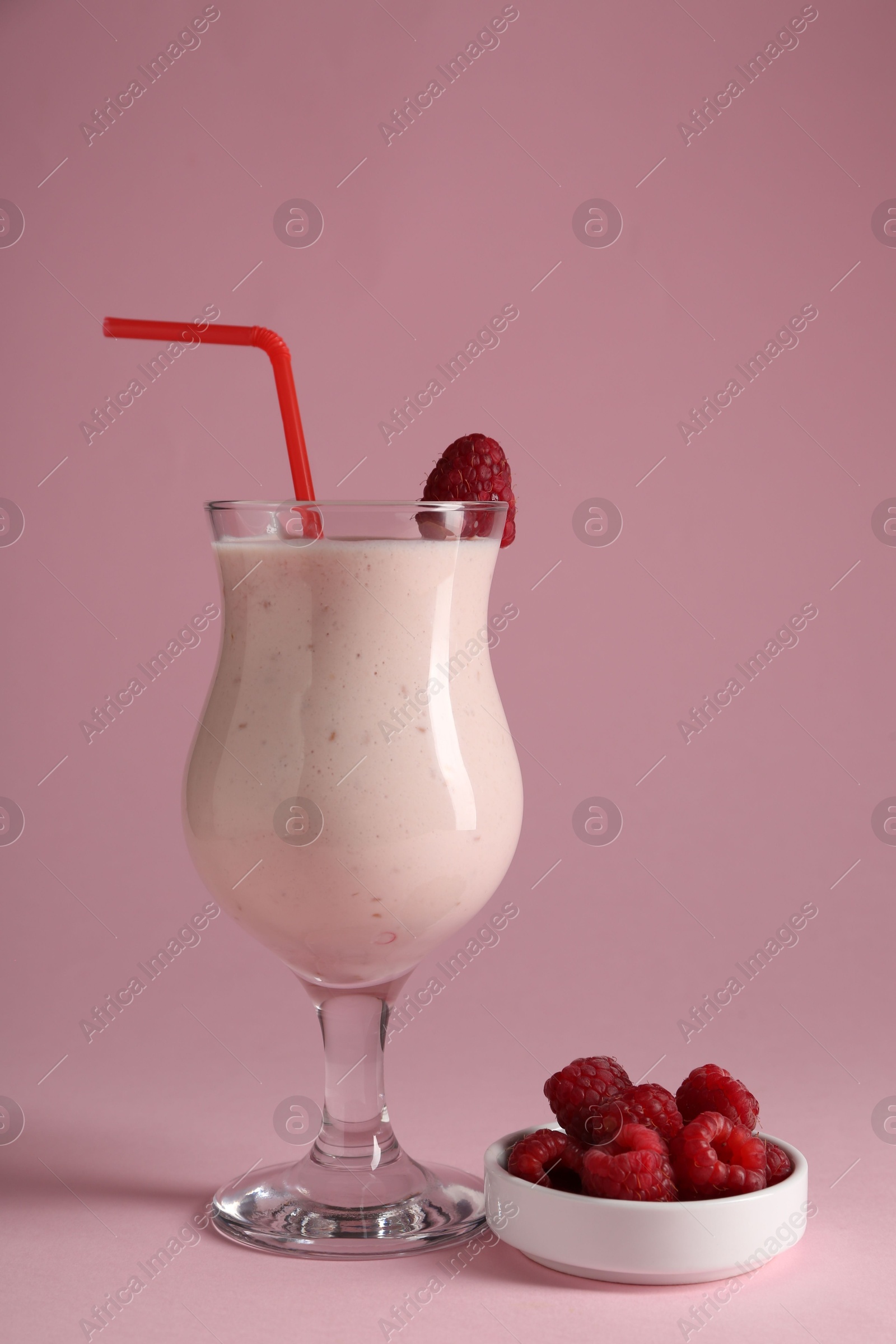 Photo of Tasty raspberry milkshake in glass and berries on pink background