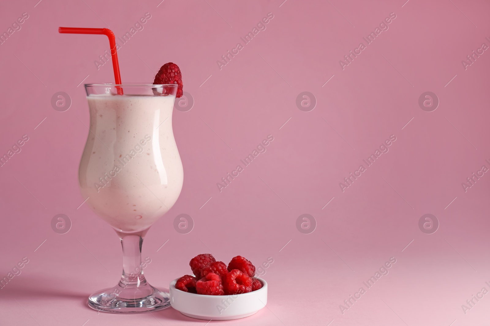 Photo of Tasty raspberry milkshake in glass and berries on pink background, space for text