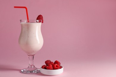 Photo of Tasty raspberry milkshake in glass and berries on pink background, space for text
