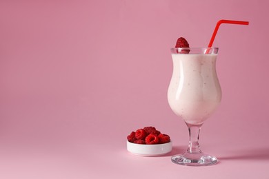 Photo of Tasty raspberry milkshake in glass and berries on pink background, space for text