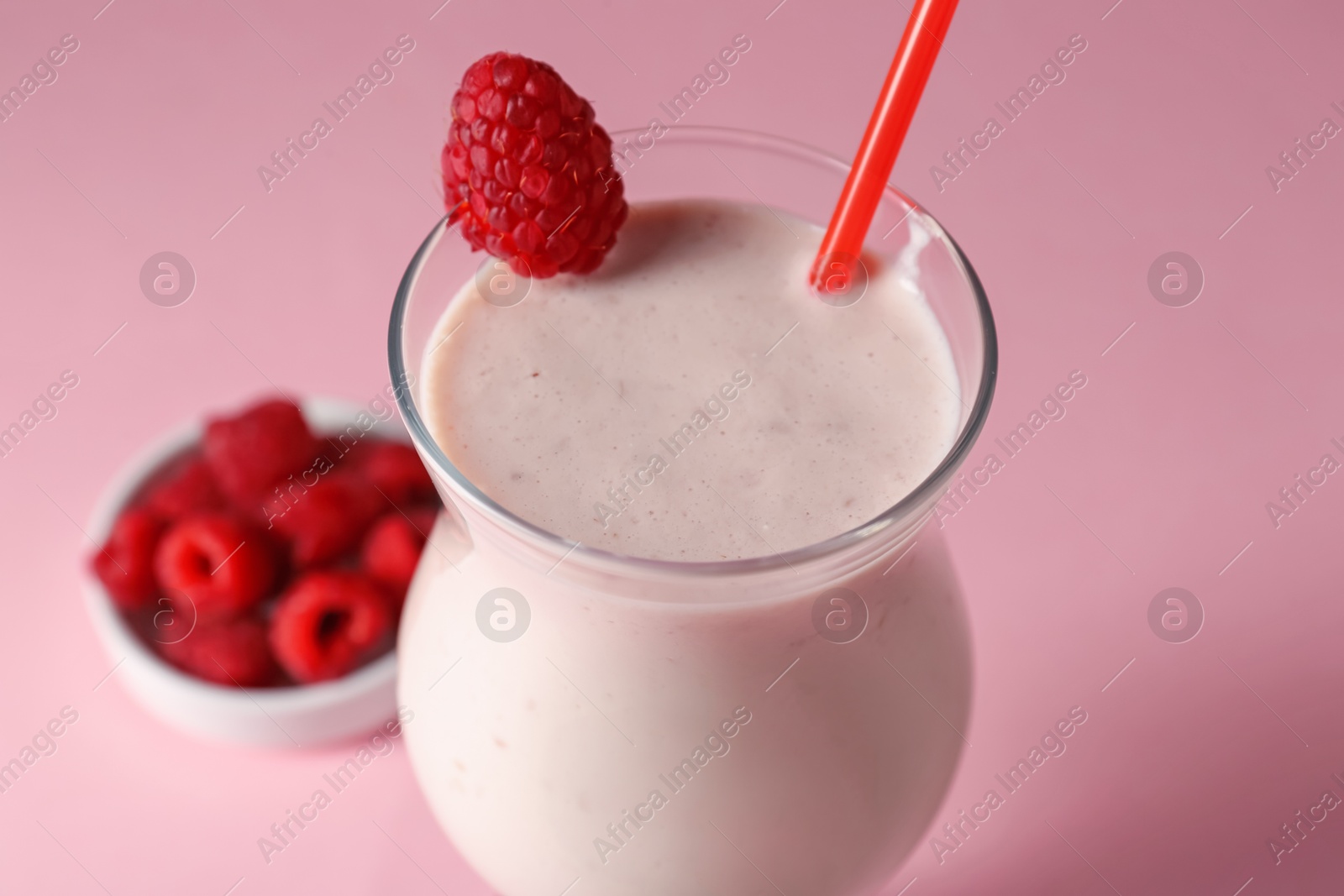 Photo of Tasty raspberry milkshake in glass and berries on pink background, closeup