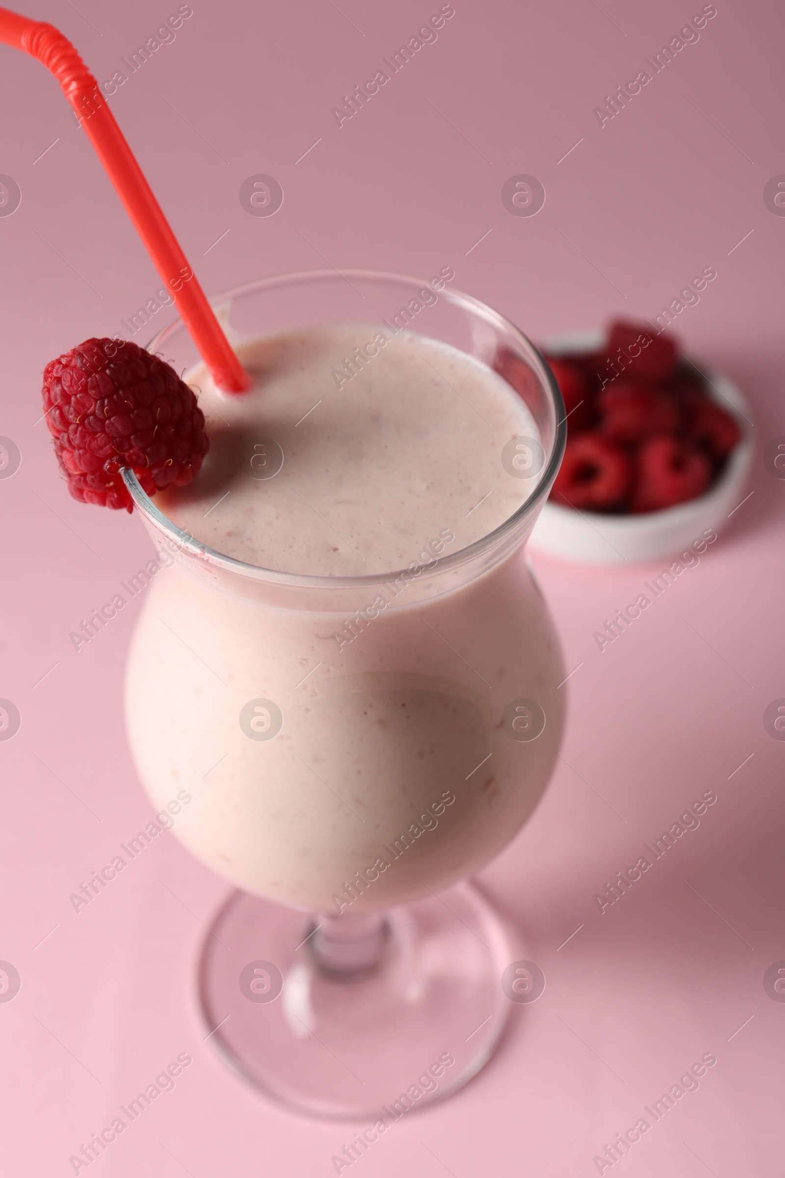 Photo of Tasty raspberry milkshake in glass and berries on pink background, closeup