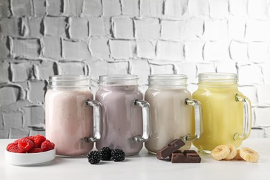Photo of Different tasty milkshakes in mason jars and ingredients on white table