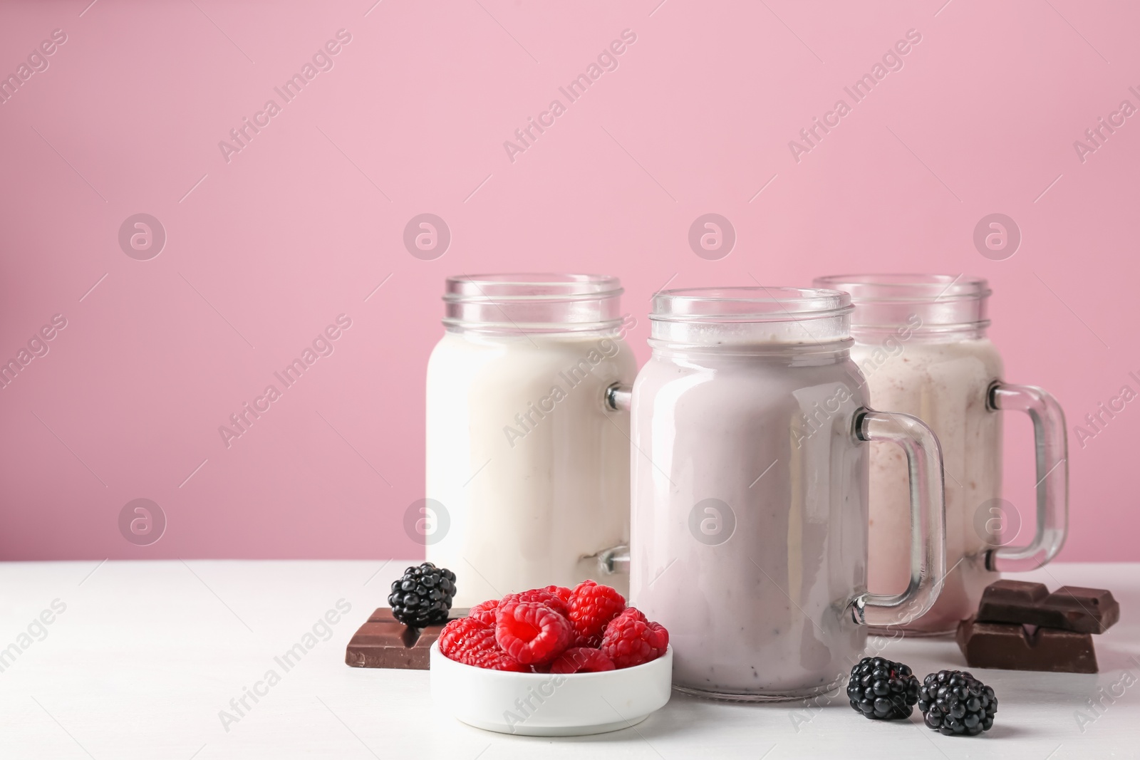 Photo of Different tasty milkshakes in mason jars and ingredients on white table, space for text