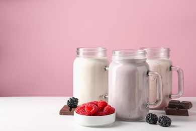Photo of Different tasty milkshakes in mason jars and ingredients on white table, space for text