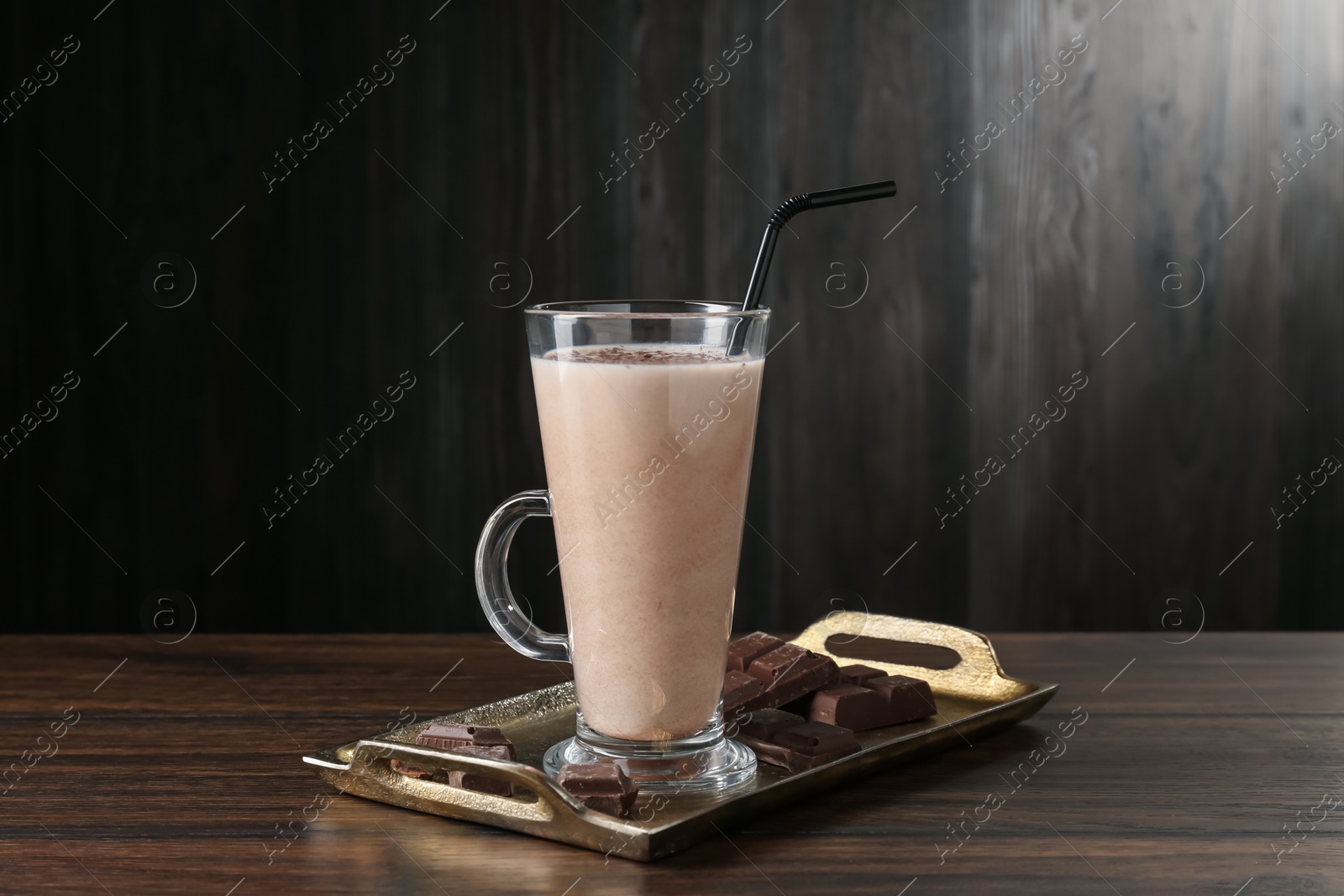 Photo of Tasty milkshake in glass and pieces of chocolate on wooden table