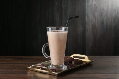 Photo of Tasty milkshake in glass and pieces of chocolate on wooden table
