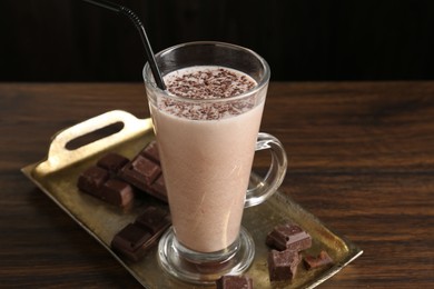 Photo of Tasty milkshake in glass and pieces of chocolate on wooden table, closeup