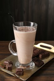 Photo of Tasty milkshake in glass and pieces of chocolate on wooden table, closeup