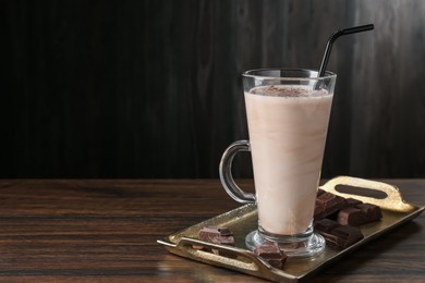 Photo of Tasty milkshake in glass and pieces of chocolate on wooden table, space for text
