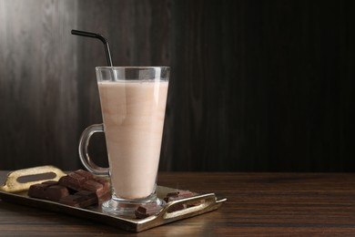 Photo of Tasty milkshake in glass and pieces of chocolate on wooden table, space for text