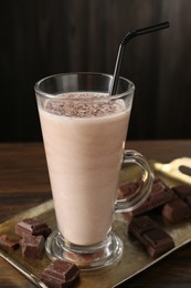 Photo of Tasty milkshake in glass and pieces of chocolate on wooden table, closeup