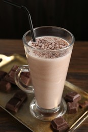 Photo of Tasty milkshake in glass and pieces of chocolate on wooden table, closeup