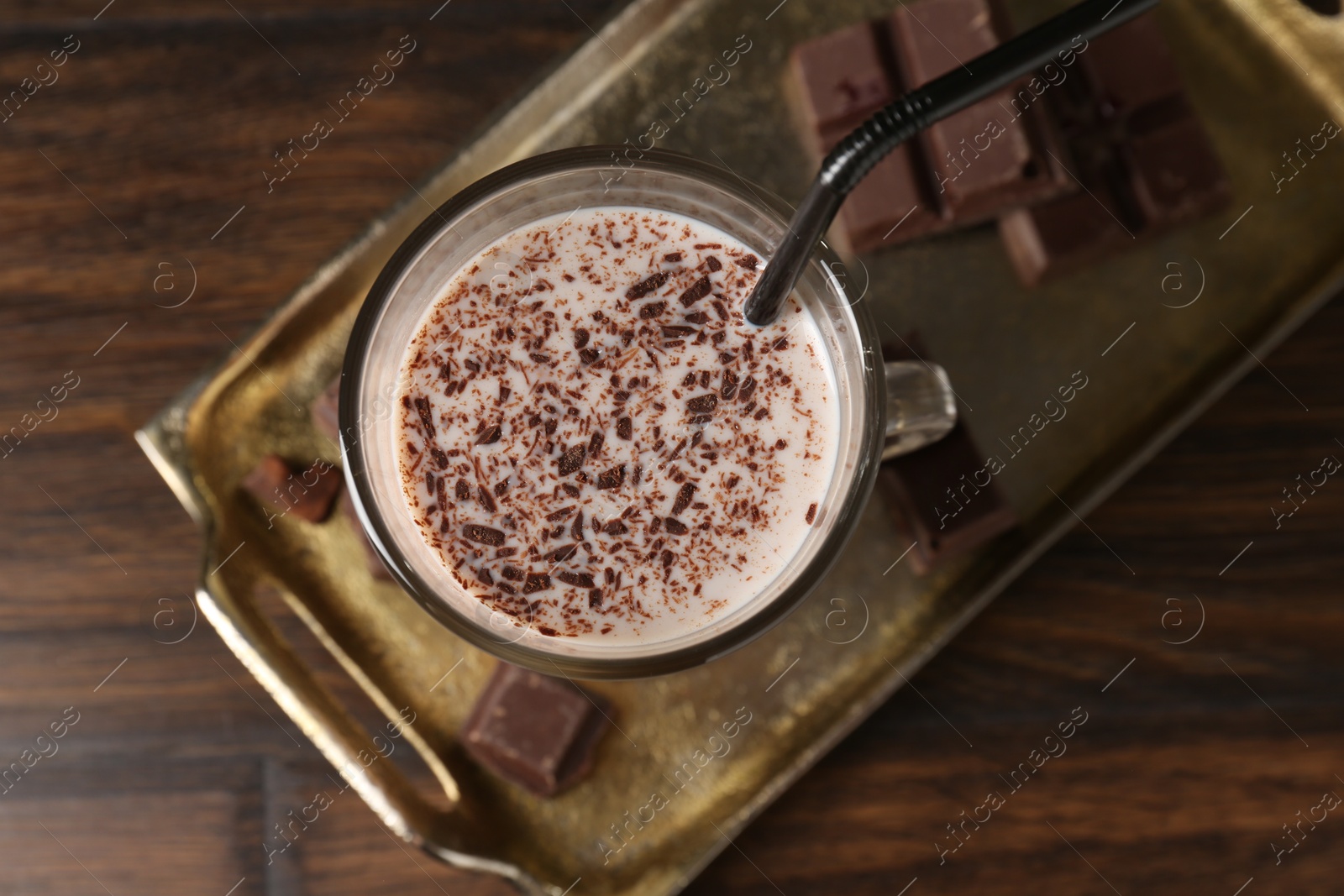 Photo of Tasty milkshake in glass and pieces of chocolate on wooden table, top view