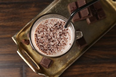 Photo of Tasty milkshake in glass and pieces of chocolate on wooden table, top view