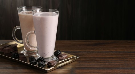 Photo of Different tasty milkshakes in glasses and ingredients on wooden table, space for text