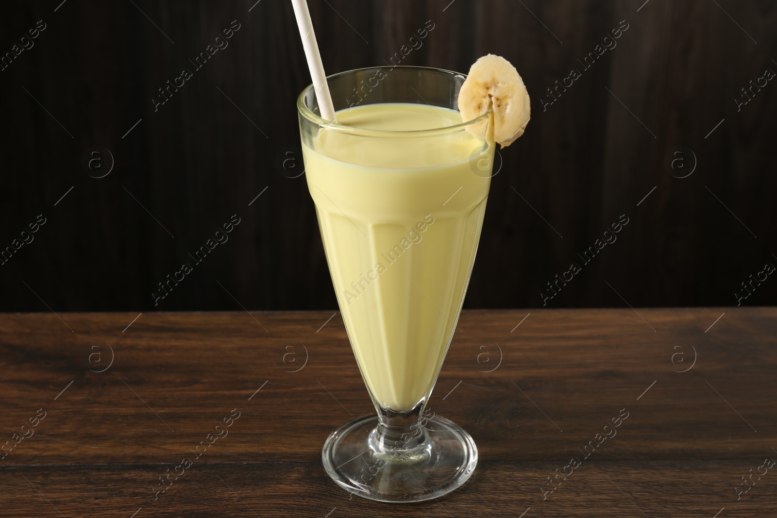 Photo of Tasty banana milkshake in glass on wooden table, closeup