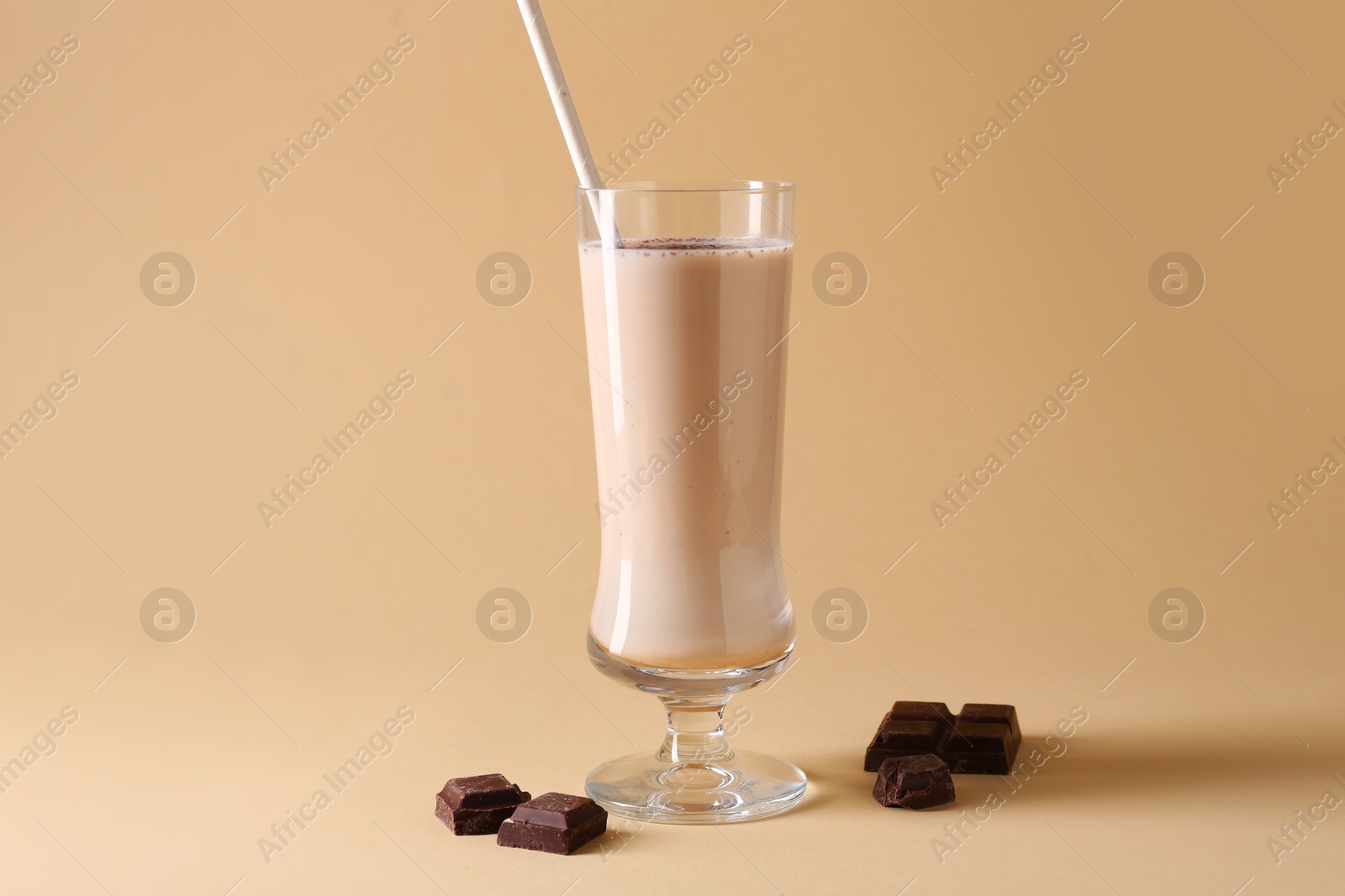 Photo of Tasty milkshake in glass and pieces of chocolate on beige background