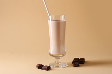Photo of Tasty milkshake in glass and pieces of chocolate on beige background