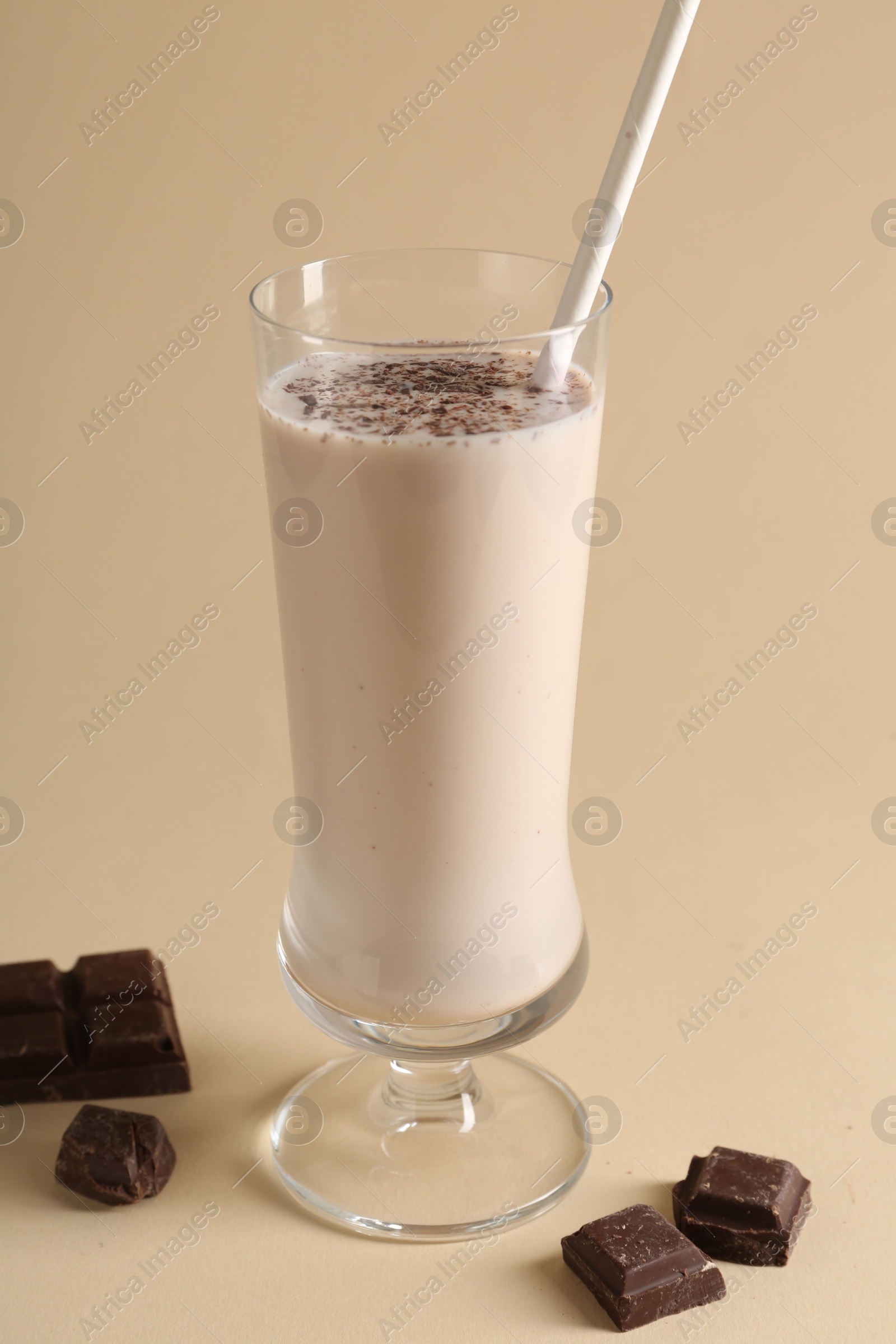 Photo of Tasty milkshake in glass and pieces of chocolate on beige background, closeup
