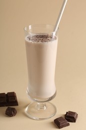 Photo of Tasty milkshake in glass and pieces of chocolate on beige background, closeup