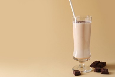 Photo of Tasty milkshake in glass and pieces of chocolate on beige background, space for text