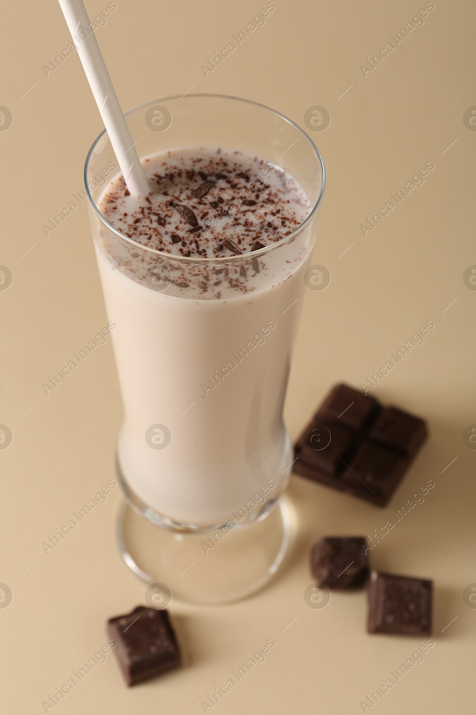 Photo of Tasty milkshake in glass and pieces of chocolate on beige background, closeup