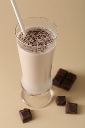 Photo of Tasty milkshake in glass and pieces of chocolate on beige background, closeup