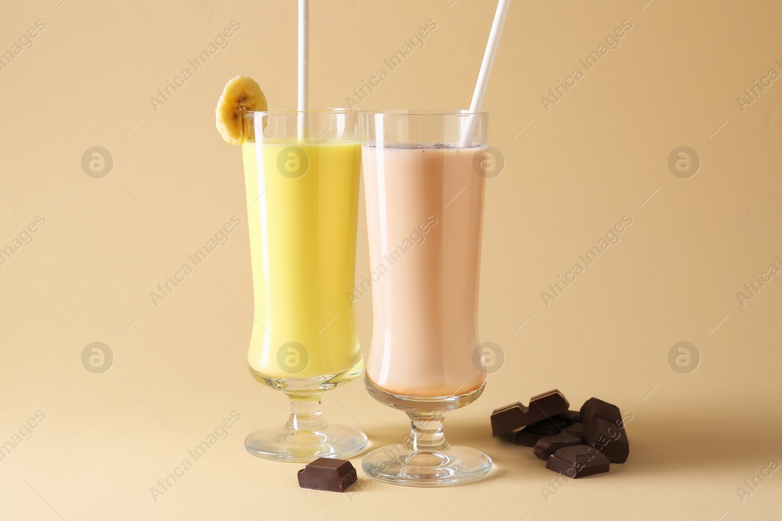 Photo of Different tasty milkshakes in glasses and pieces of chocolate on beige background