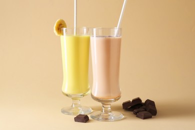 Photo of Different tasty milkshakes in glasses and pieces of chocolate on beige background