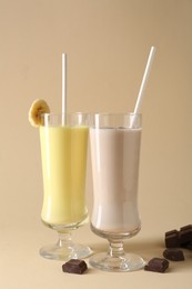 Photo of Different tasty milkshakes in glasses and pieces of chocolate on beige background